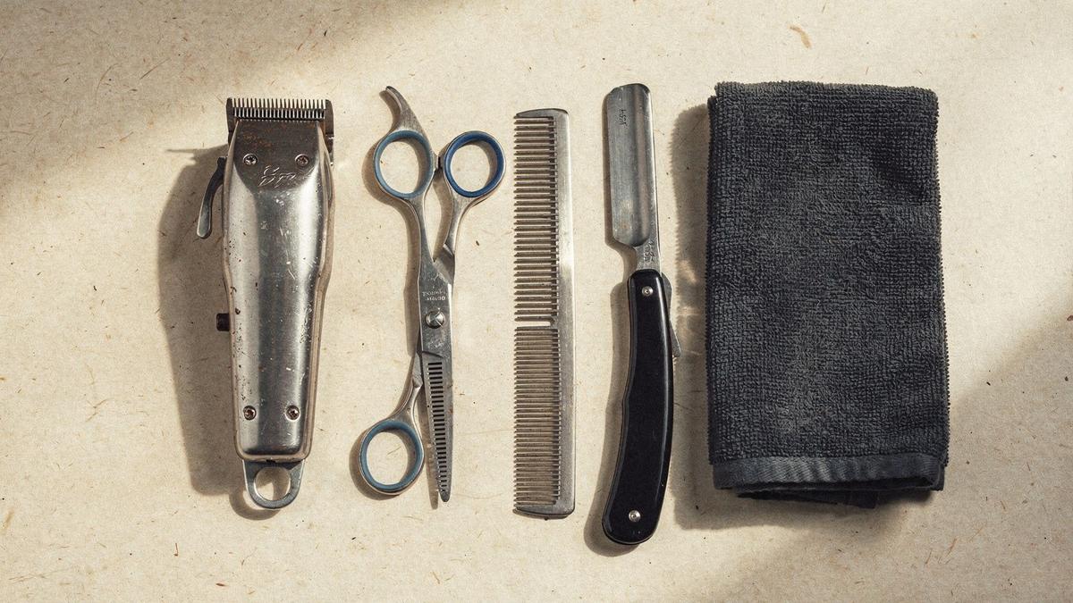 Barber workbench with clippers, scissors, comb and straight razor arranged on a folded towel